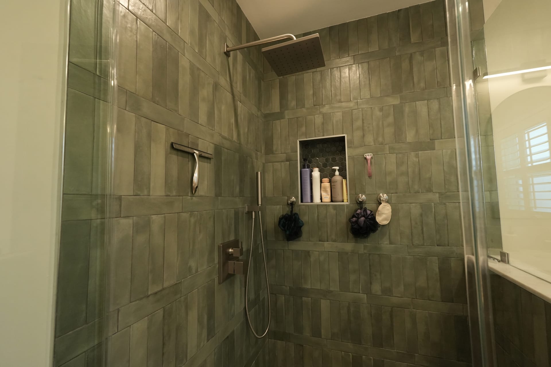 tiled shower with dark wall tile, shower niche, and glass door