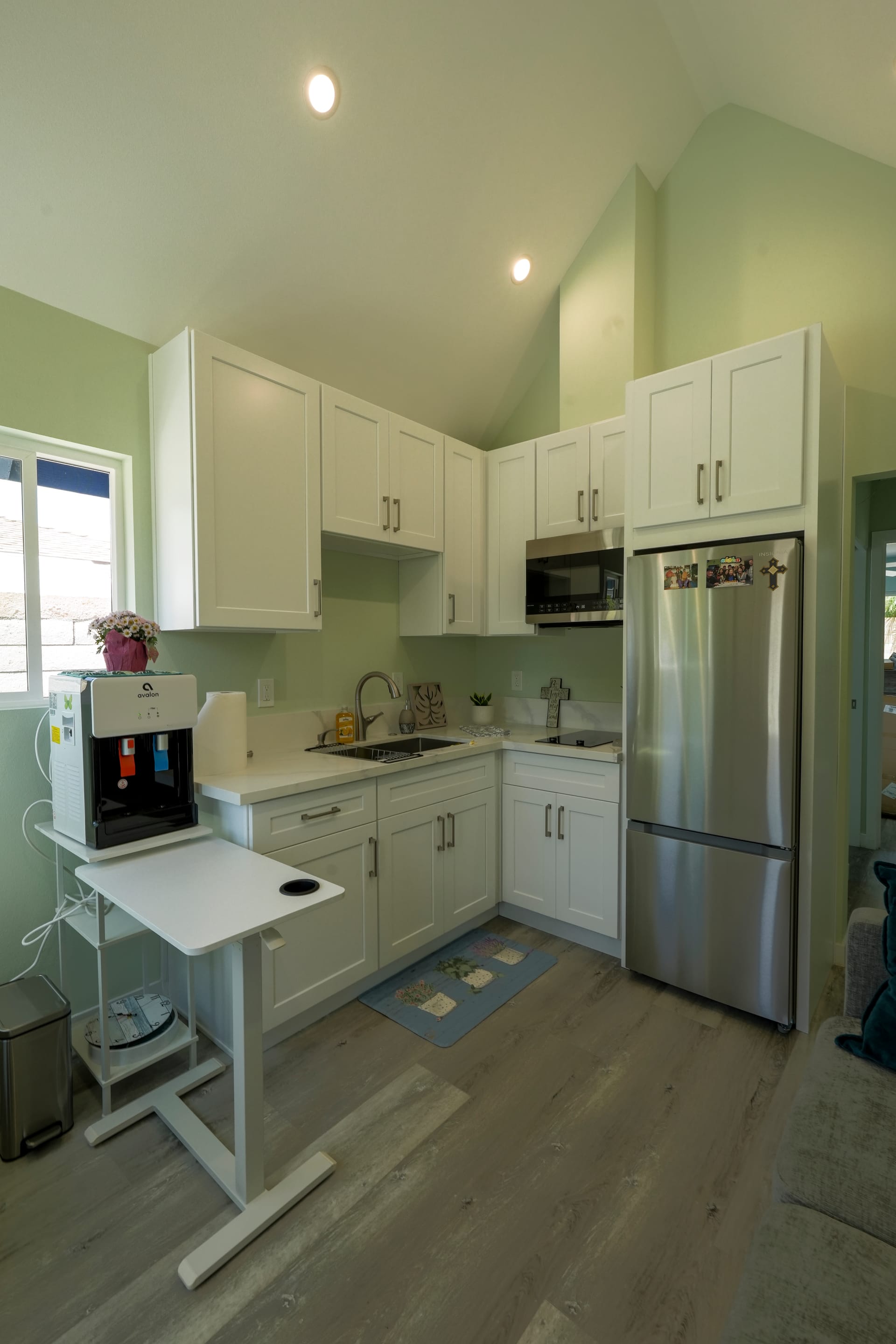 white kitchen with island cart, sink, upper cabinets, and stainless refrigerator