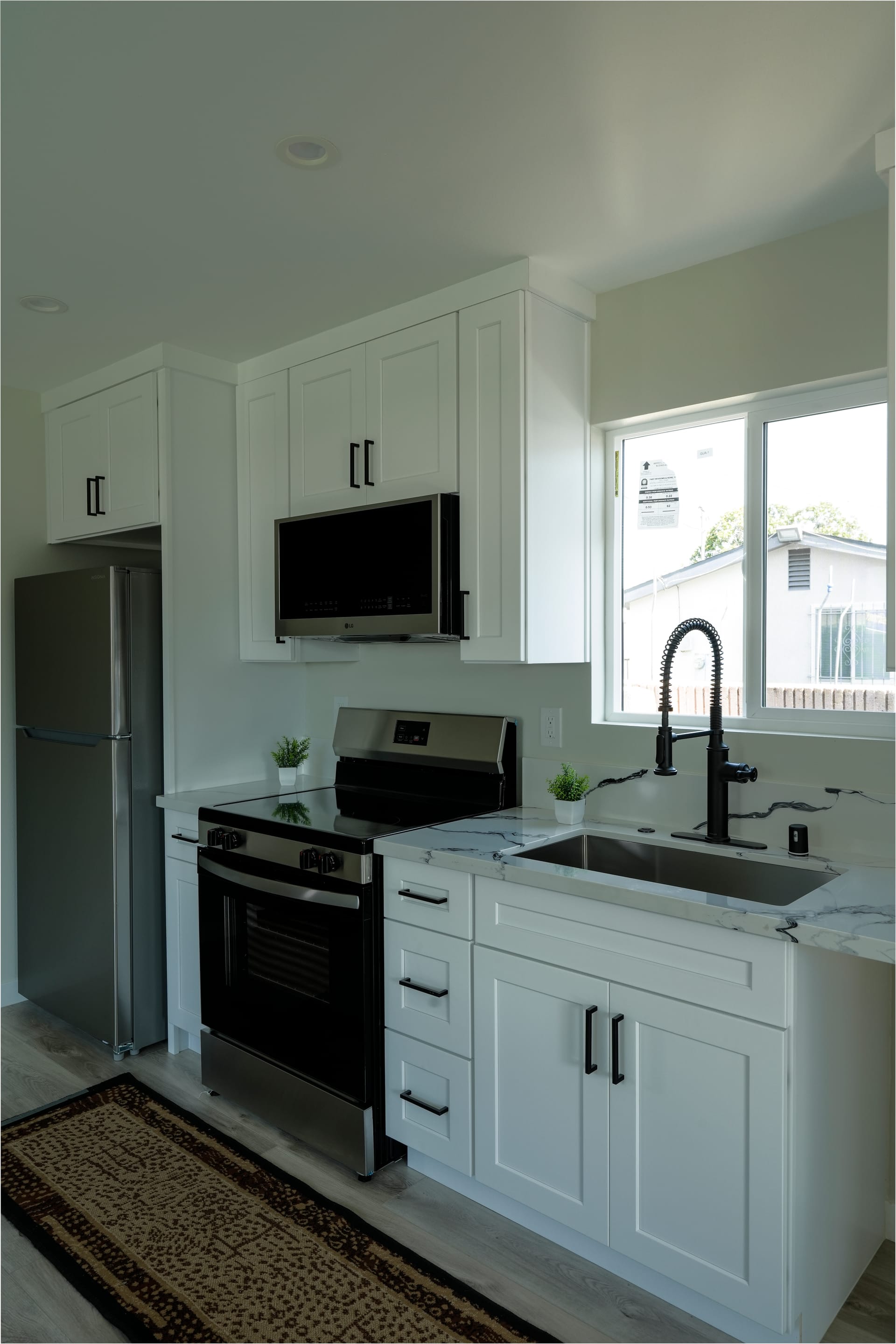 white kitchen with stainless steel refrigerator, black range, microwave, and island sink