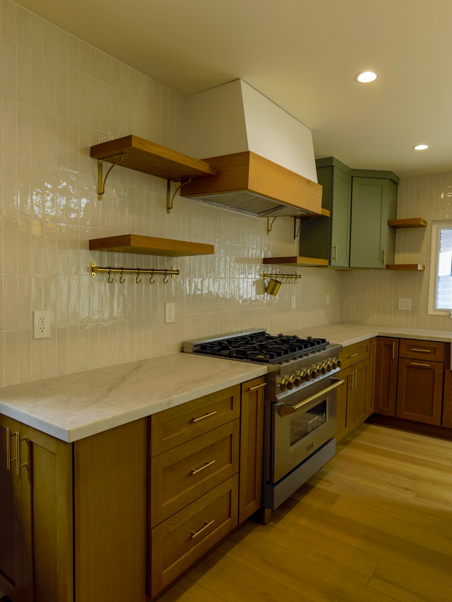 Kitchen range beneath a wood hood with green lower cabinets