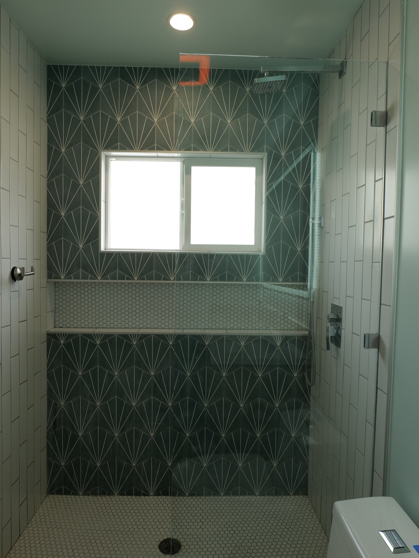 Glass shower with green tile and a high window